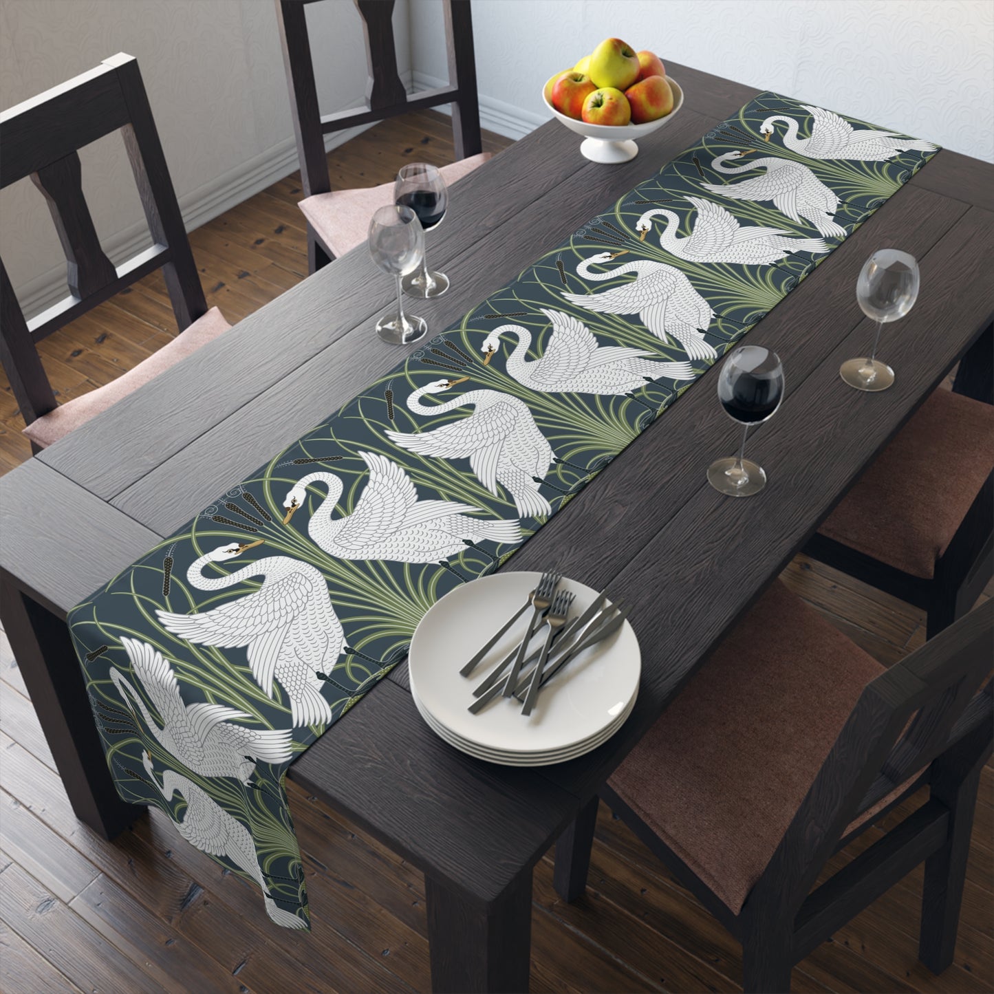 Dining table with a swan patterned table runner, plates, and glasses.