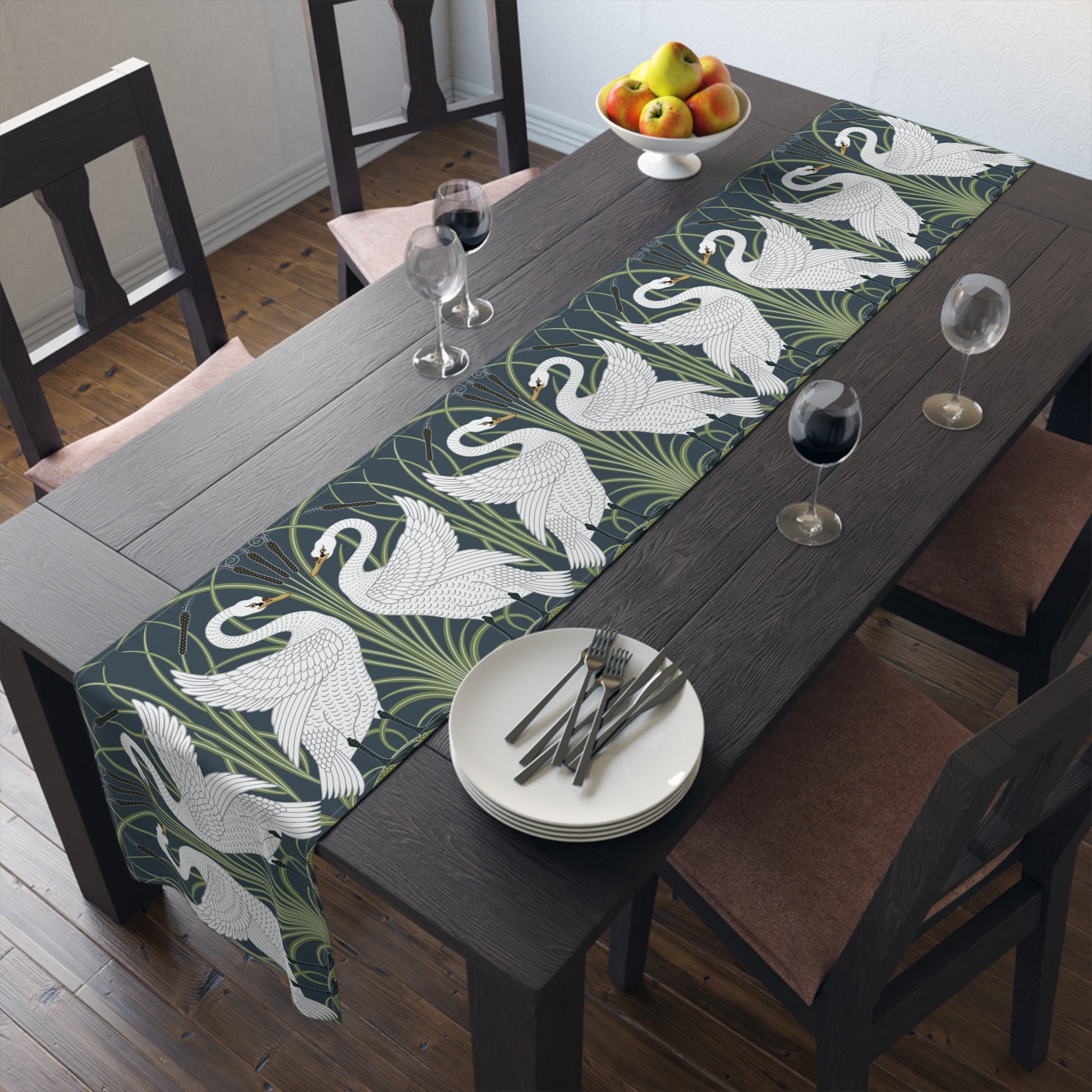 Dining table with a swan patterned table runner, plates, and glasses.