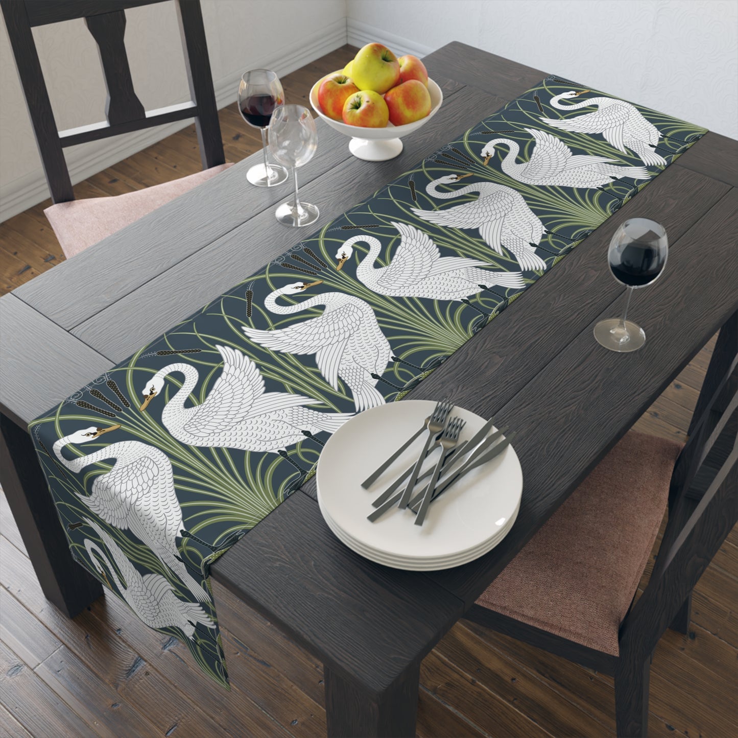 Dining table with a swan patterned table runner, plates, and fruit.