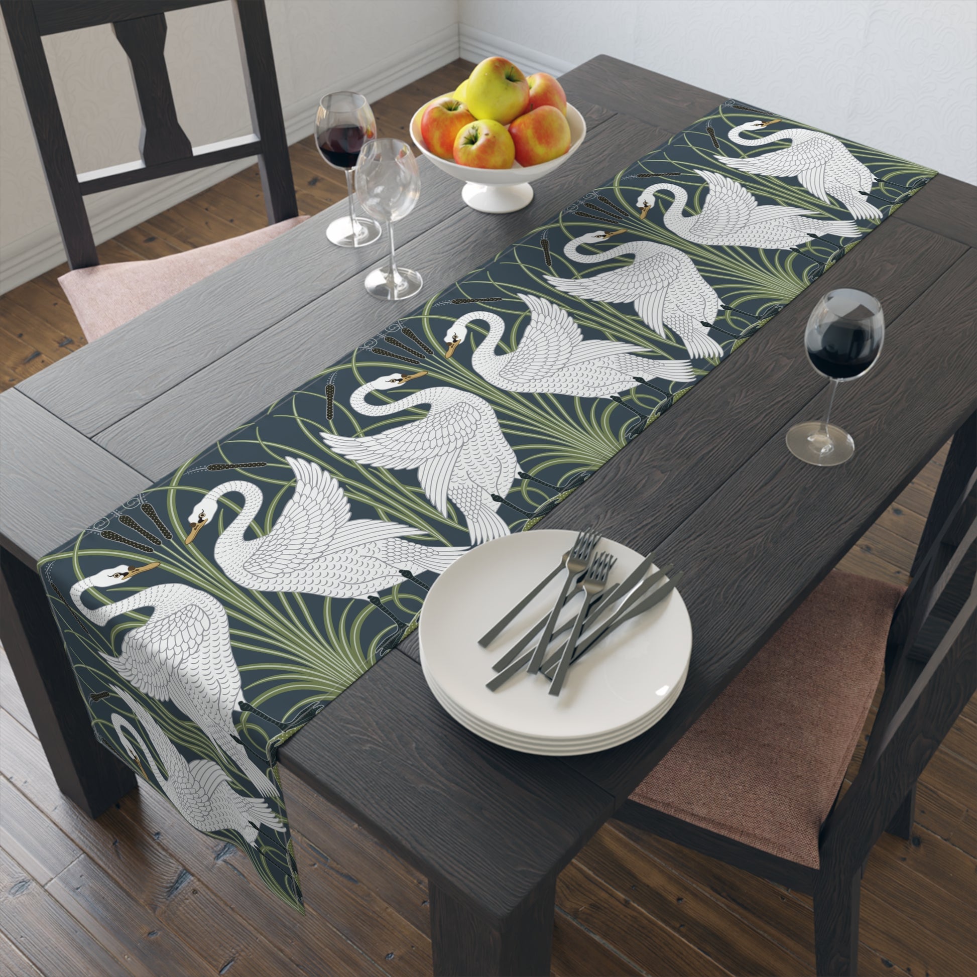 Dining table with a swan patterned table runner, plates, and fruit.