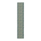 A table runner with a green and gold William Morris & Co pattern displayed on a dining table setting with dishes and glasses.