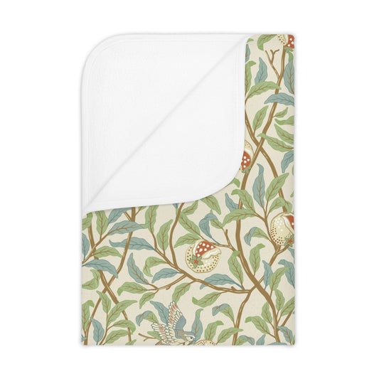 A toddler blanket with a floral pattern featuring birds and pomegranates in green, red, and beige colors on a parchment background.