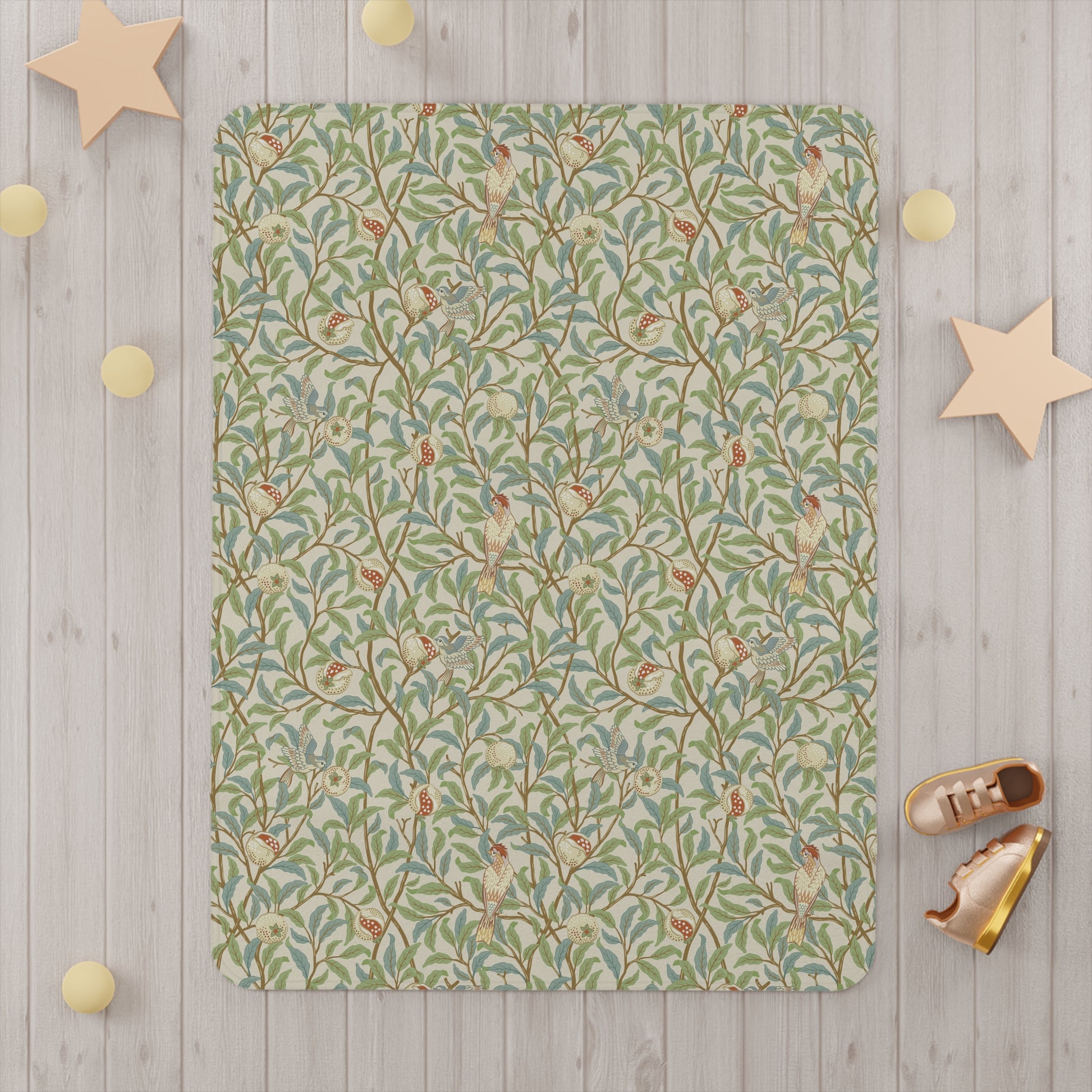 A toddler blanket with a floral pattern featuring birds and pomegranates in green, red, and beige colours on a parchment background.