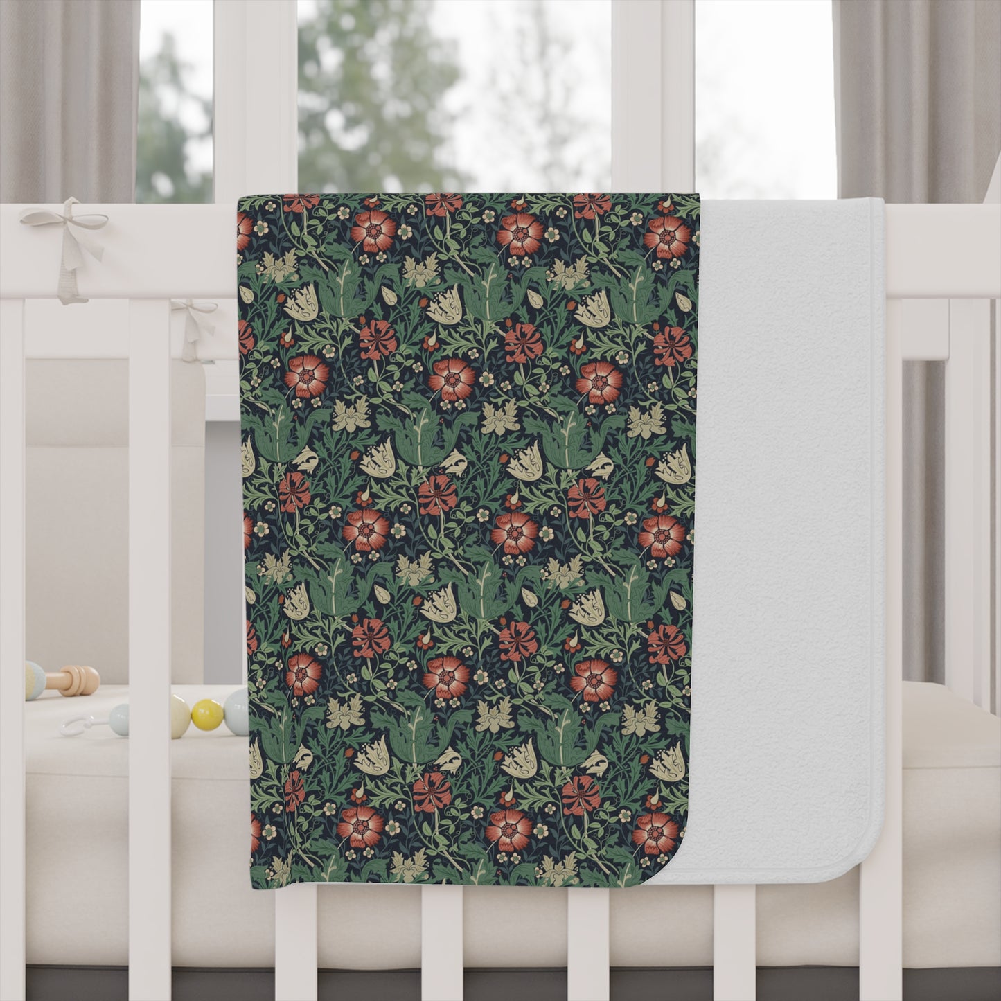 Floral patterned blanket draped over a crib with a white crib and curtains in the background.