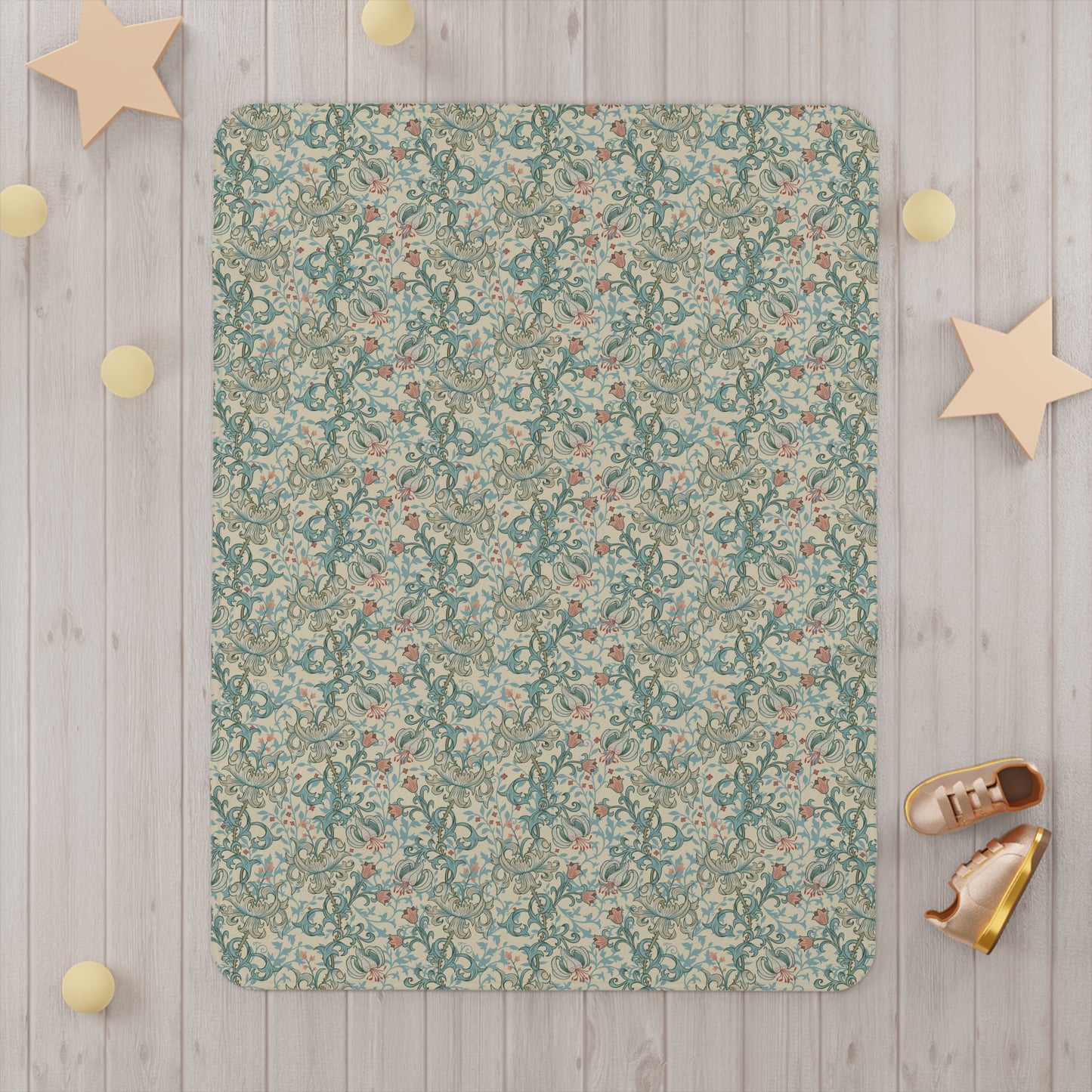 Floral patterned baby blanket on a wooden floor with decorative stars and shoes around it.