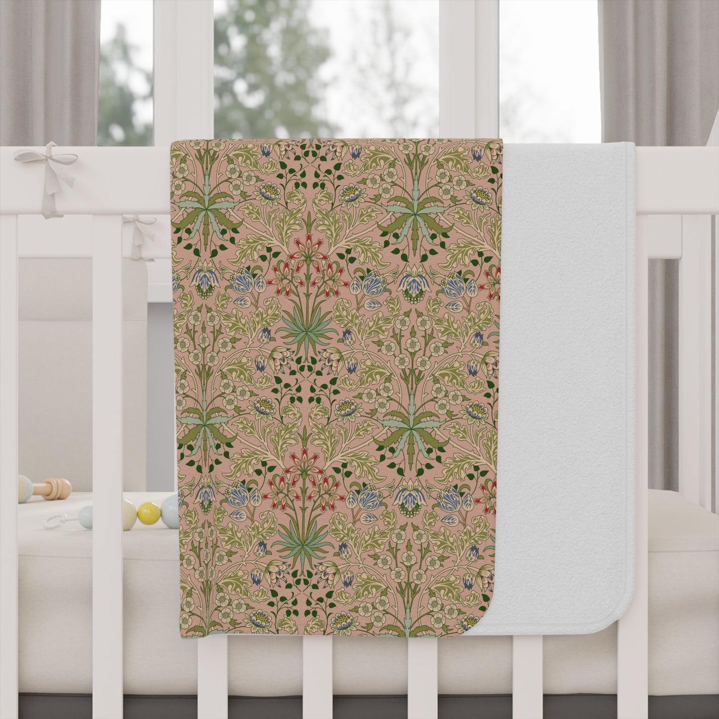 A toddler blanket with a floral pattern inspired by William Morris, in shades of green, pink, and blue on a beige background.