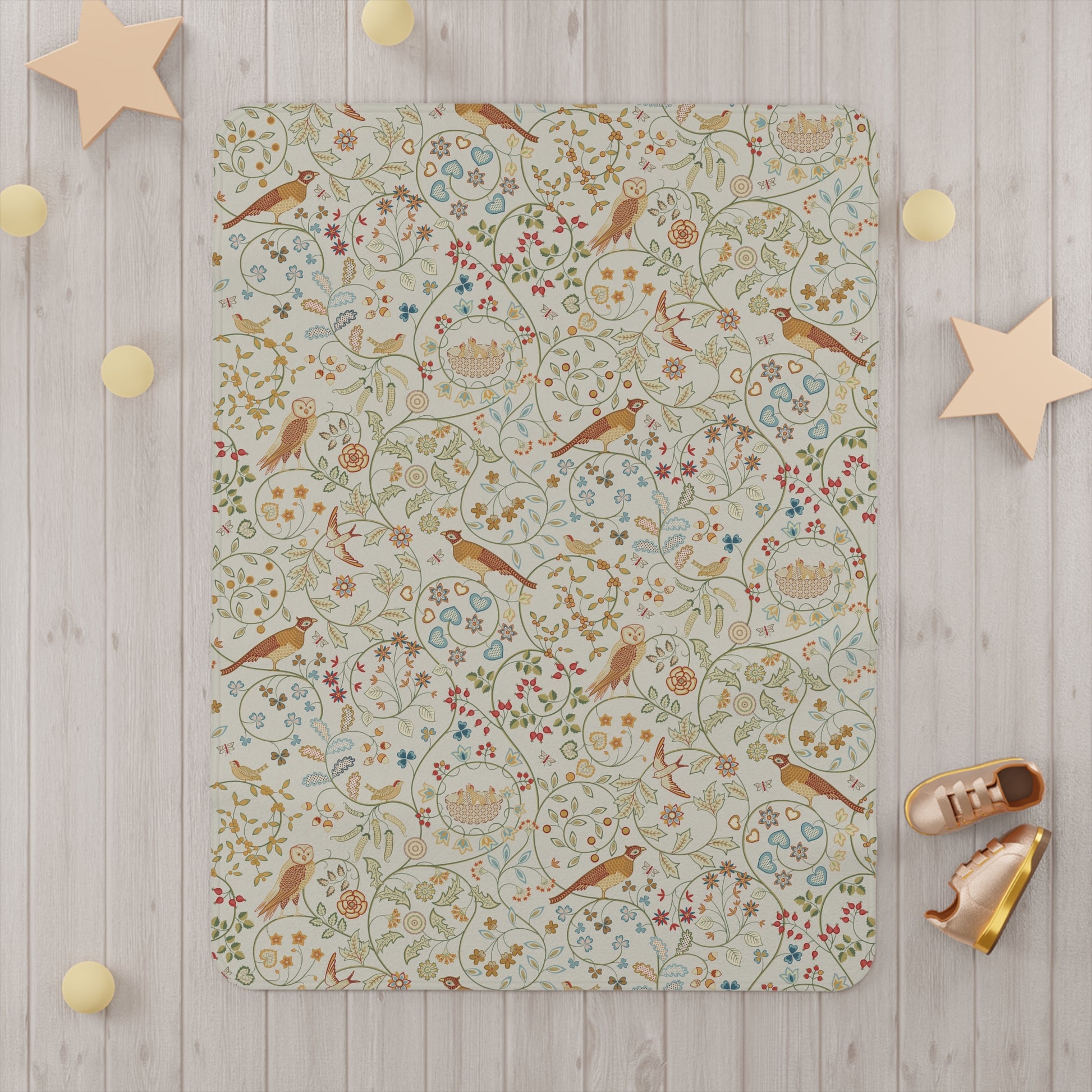A toddler blanket with a floral and bird pattern inspired by William Morris, in vibrant colours on a light background, folded neatly.