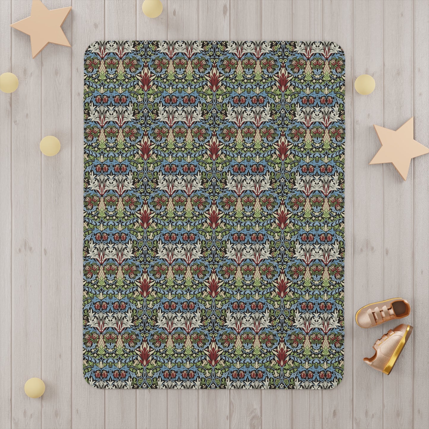 A toddler blanket with a floral pattern inspired by William Morris, featuring colours predominantly in blue, green, and red, with a mix of geometric and organic shapes.