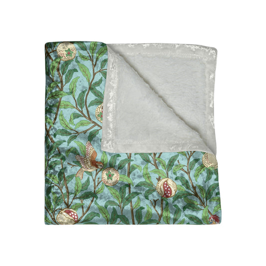 A crushed velvet blanket with a floral pattern in shades of blue and green, featuring birds and pomegranate designs, displayed on a flat surface.