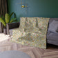 Floral-patterned blanket draped over a sofa in a living room with a green wall and plant.