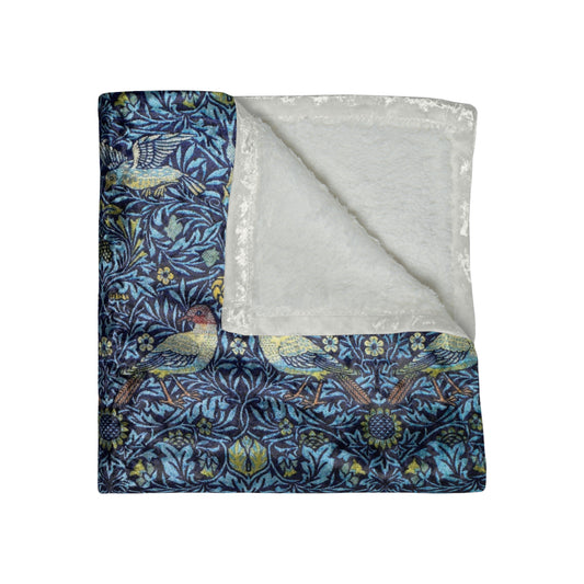 A lush crushed velvet blanket with a blue floral William Morris & Co pattern on the surface and a silky finish, hemmed edges, and a white interior visible at one end.