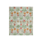 A lush crushed velvet blanket with a pattern inspired by William Morris, featuring daisy motifs in a green, red, and white color palette on a gray background.