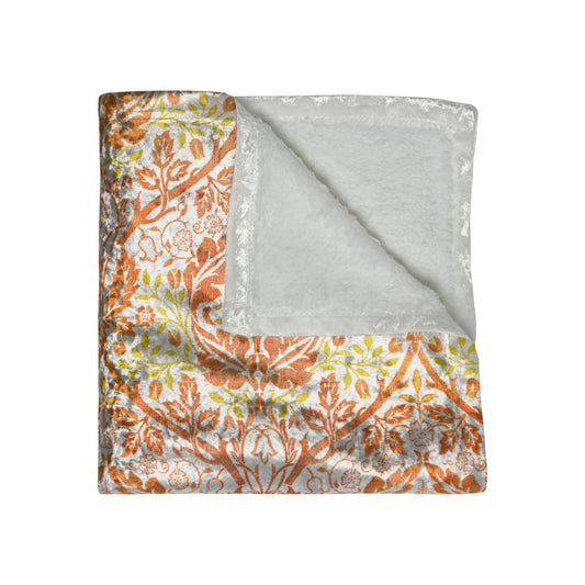 A crushed velvet blanket with a William Morris & Co floral pattern in shades of orange, yellow, and green on a white background, folded to show both the patterned side and the solid silky finish.