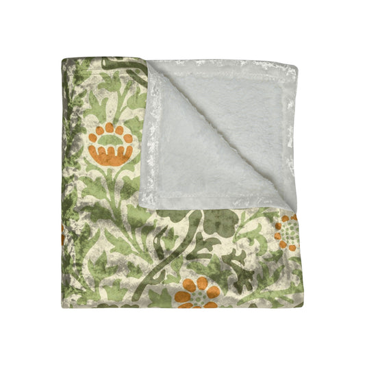 A plush, velvet blanket with aWilliam Morris  floral pattern in shades of green and orange, folded to show both the front and back with hemmed edges.