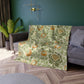 A plush, velvet blanket with aWilliam Morris  floral pattern in shades of green and orange, folded to show both the front and back with hemmed edges.