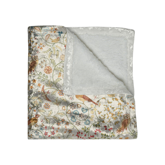 A plush, floral patterned velvet blanket in shades of green, pink, and brown with hemmed edges.