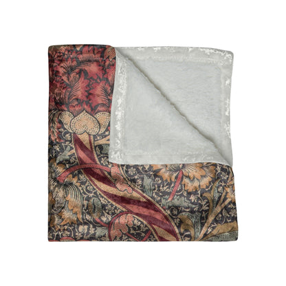 A crushed velvet blanket with a William Morris floral pattern in red and green colours, laid flat with hemmed edges visible.