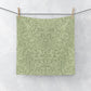Green washcloth with a leaf pattern hanging on a clothesline against a white background