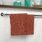 Red floral patterned towel hanging on a rack with a bathroom setting in the background.