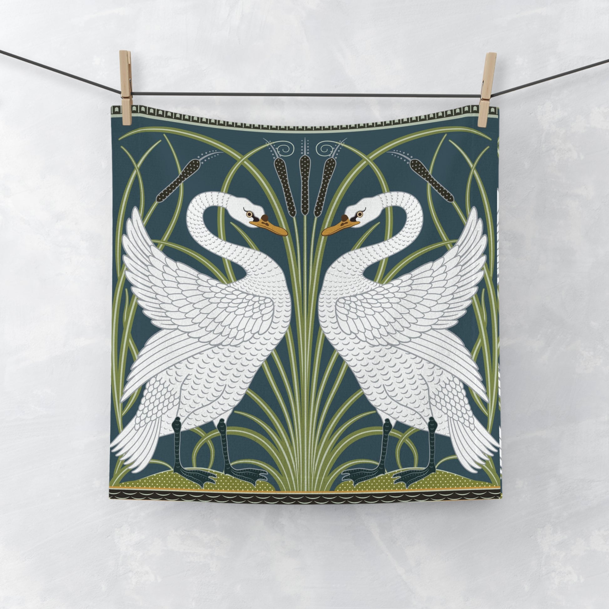 Decorative towel with white swan design on a green background, hanging on a line.