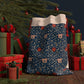 A Christmas Santa Sack with a navy background featuring an intricate floral pattern in white and red, with a cream-coloured top and red drawstrings.
