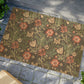 A rectangular coconut coir doormat with a floral pattern inspired by William Morris's designs, featuring a green background with multi-coloured flowers.