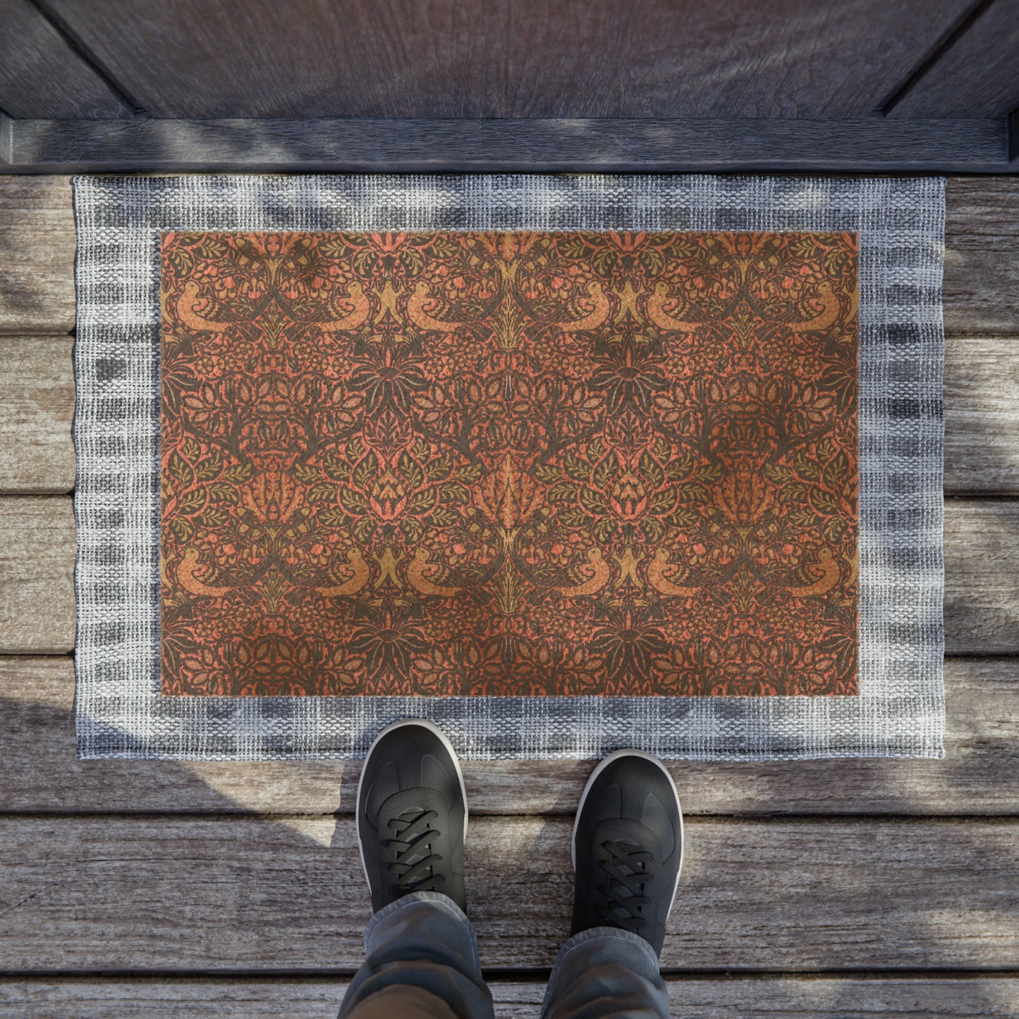 A rectangular coconut coir doormat with an intricate floral and bird William Morris & Co pattern design, primarily in pink, purple and brown colours.