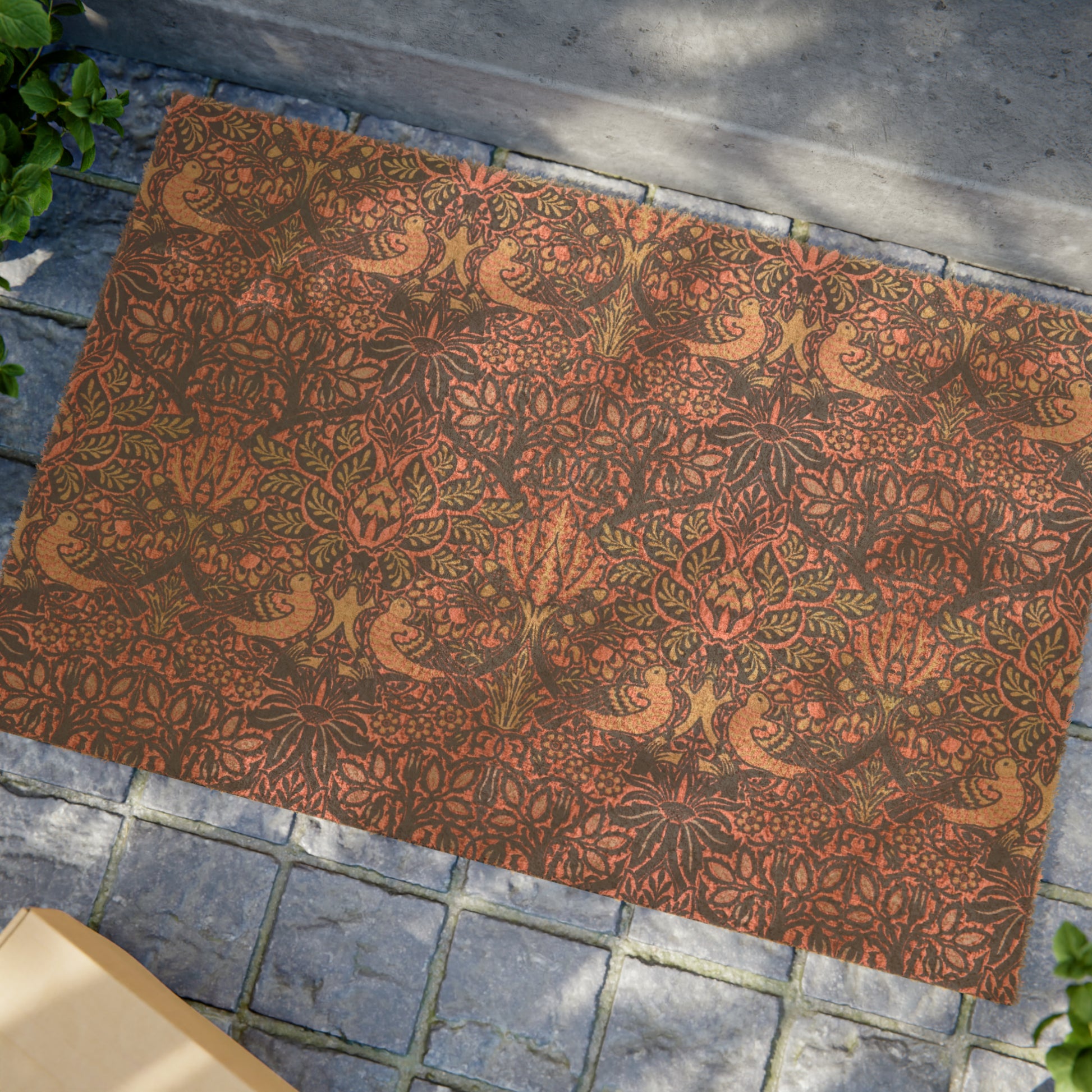 A rectangular coconut coir doormat with an intricate floral and bird William Morris & Co pattern design, primarily in pink, purple and brown colours.
