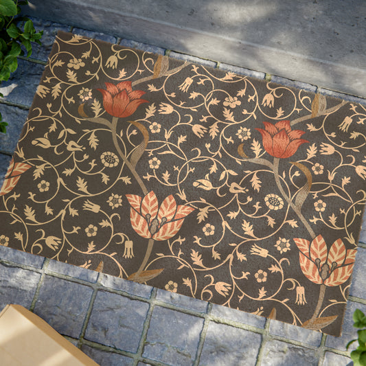 A rectangular coconut coir doormat with an intricate floral William Morris & Co pattern design, featuring a combination of dark and lighter shades, and a visible brush border at the top.