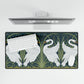 A rectangular desk mat with a floral and swan William Morris & Co pattern design, featuring a white background and swans, placed under a white mouse pad with a keyboard on top.