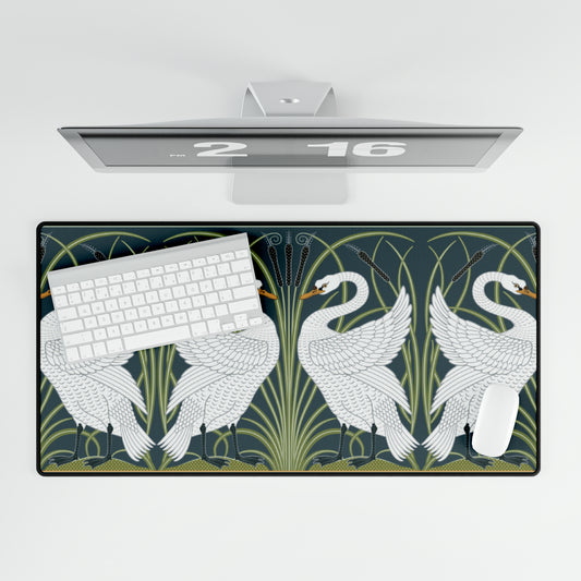 A rectangular desk mat with a floral and swan William Morris & Co pattern design, featuring a white background and swans, placed under a white mouse pad with a keyboard on top.