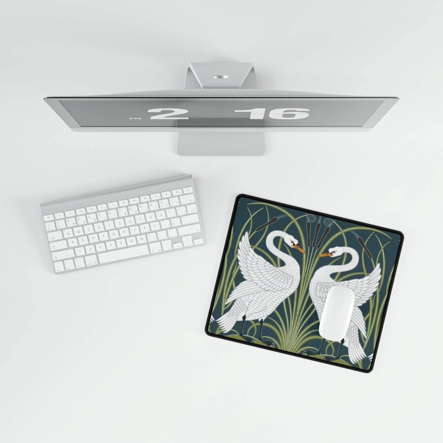 A rectangular desk mat with a floral and swan William Morris & Co pattern design, featuring a white background and swans, placed under a white mouse pad with a keyboard on top.