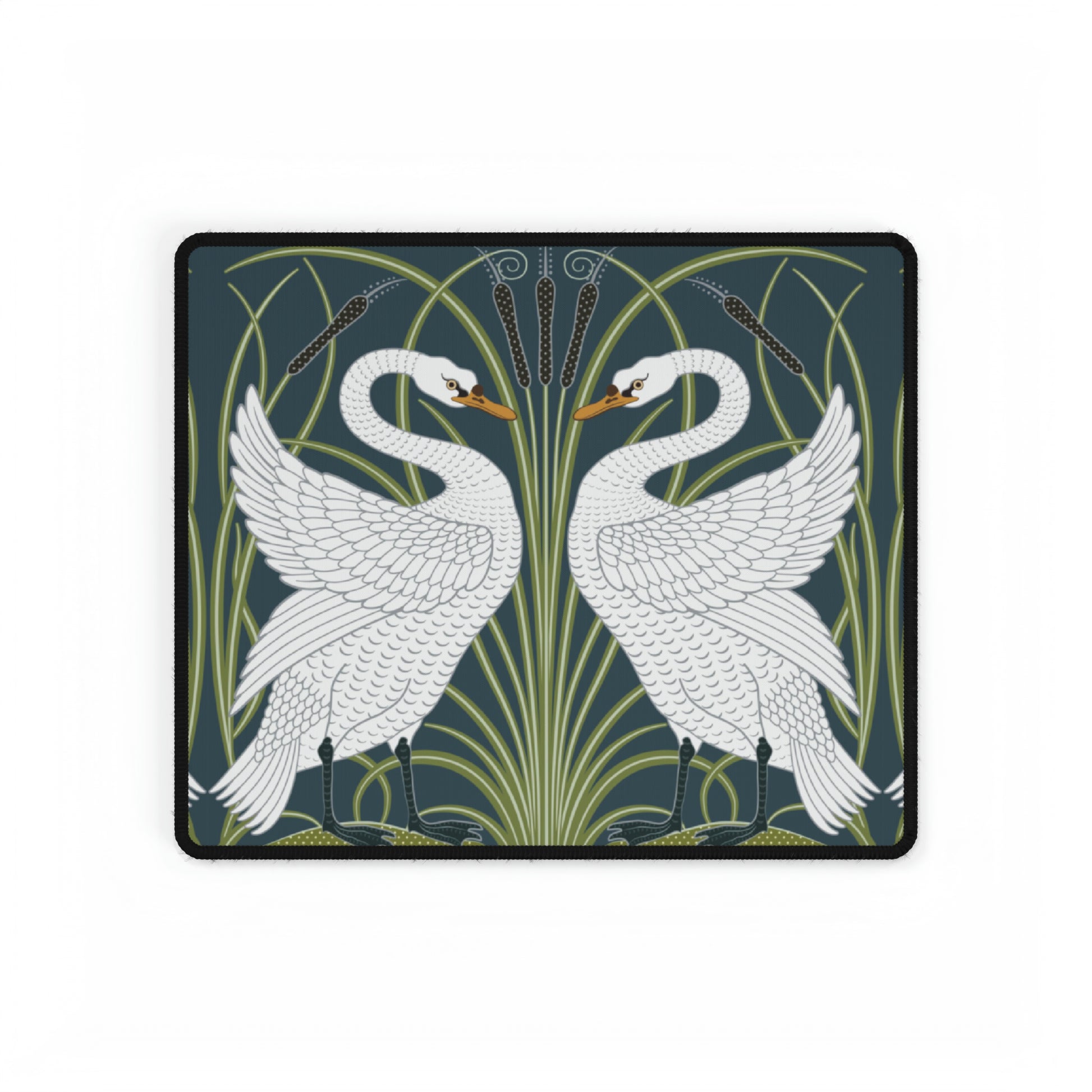 A rectangular desk mat with a floral and swan William Morris & Co pattern design, featuring a white background and swans, placed under a white mouse pad with a keyboard on top.