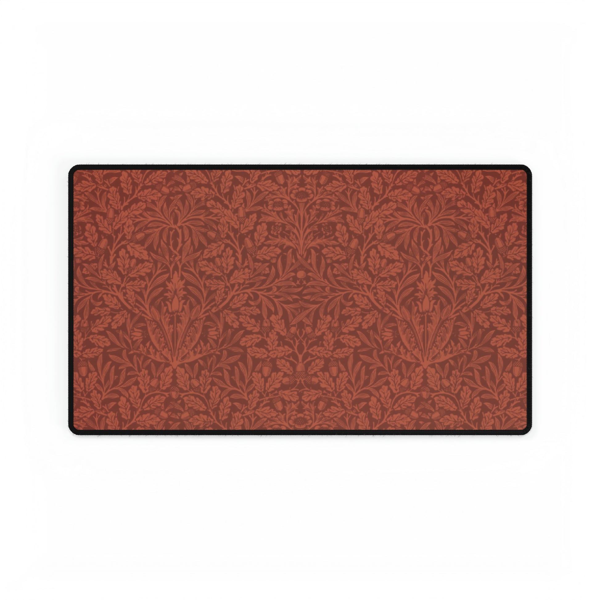 A large desk mat with a floral pattern in brown tones, displayed on a desk with a keyboard and mouse, with a monitor above it showing the time.