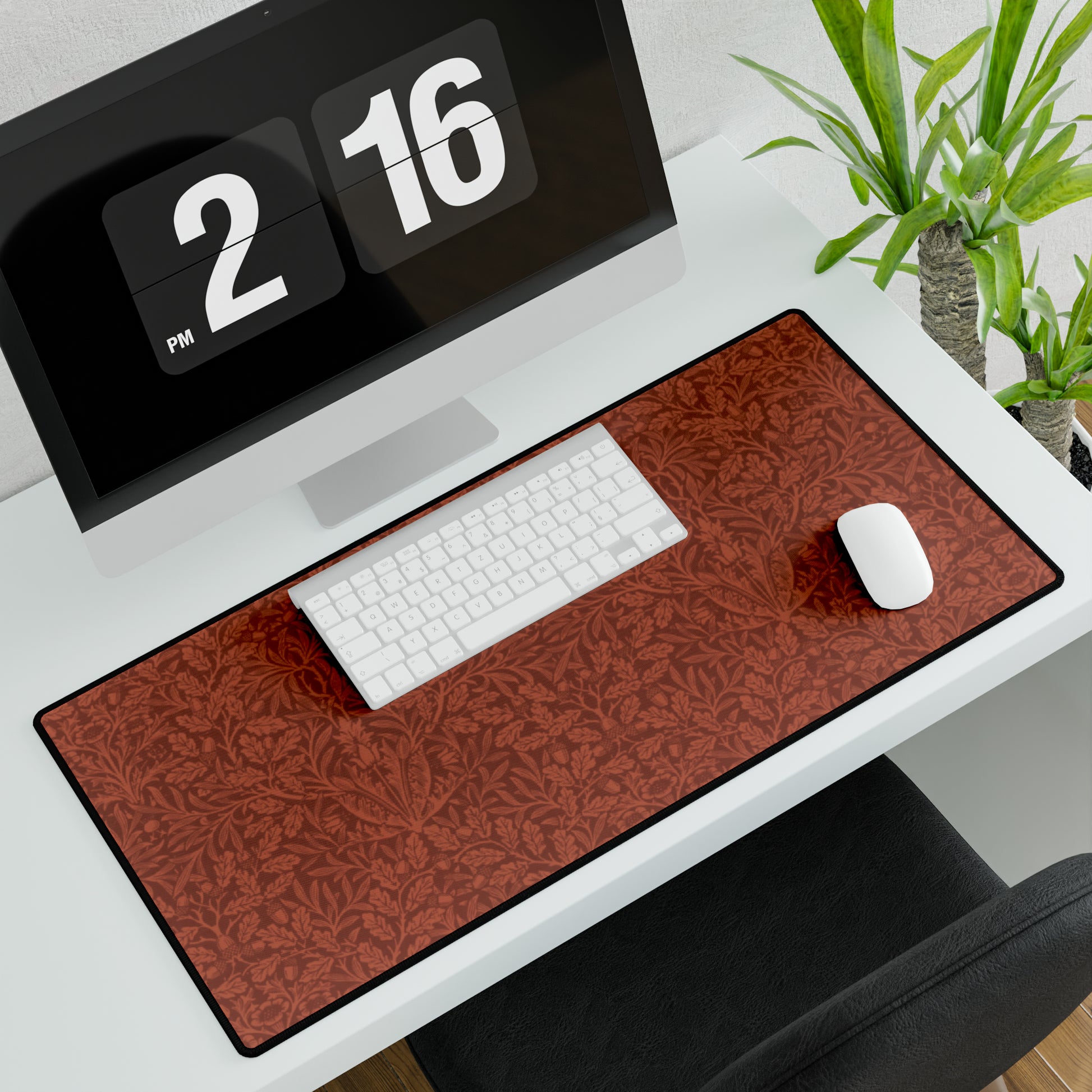 A large desk mat with a floral pattern in brown tones, displayed on a desk with a keyboard and mouse, with a monitor above it showing the time.