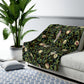 A Sherpa fleece blanket with a floral William Morris & Co pattern featuring birds and pomegranates, predominantly in green tones.
