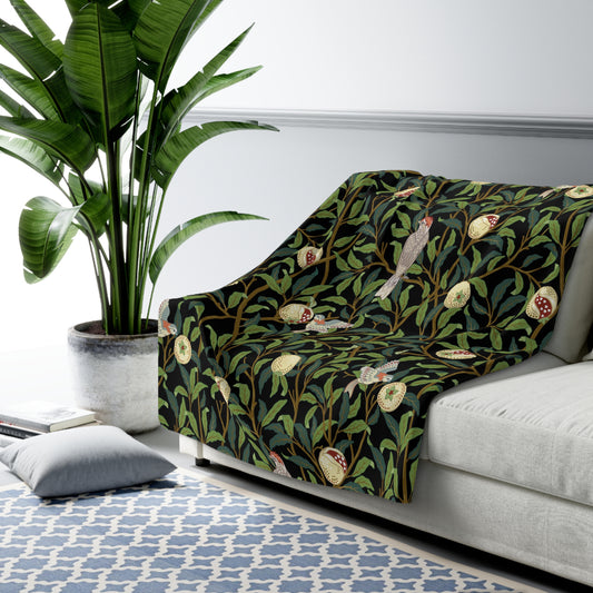 A Sherpa fleece blanket with a floral William Morris & Co pattern featuring birds and pomegranates, predominantly in green tones.