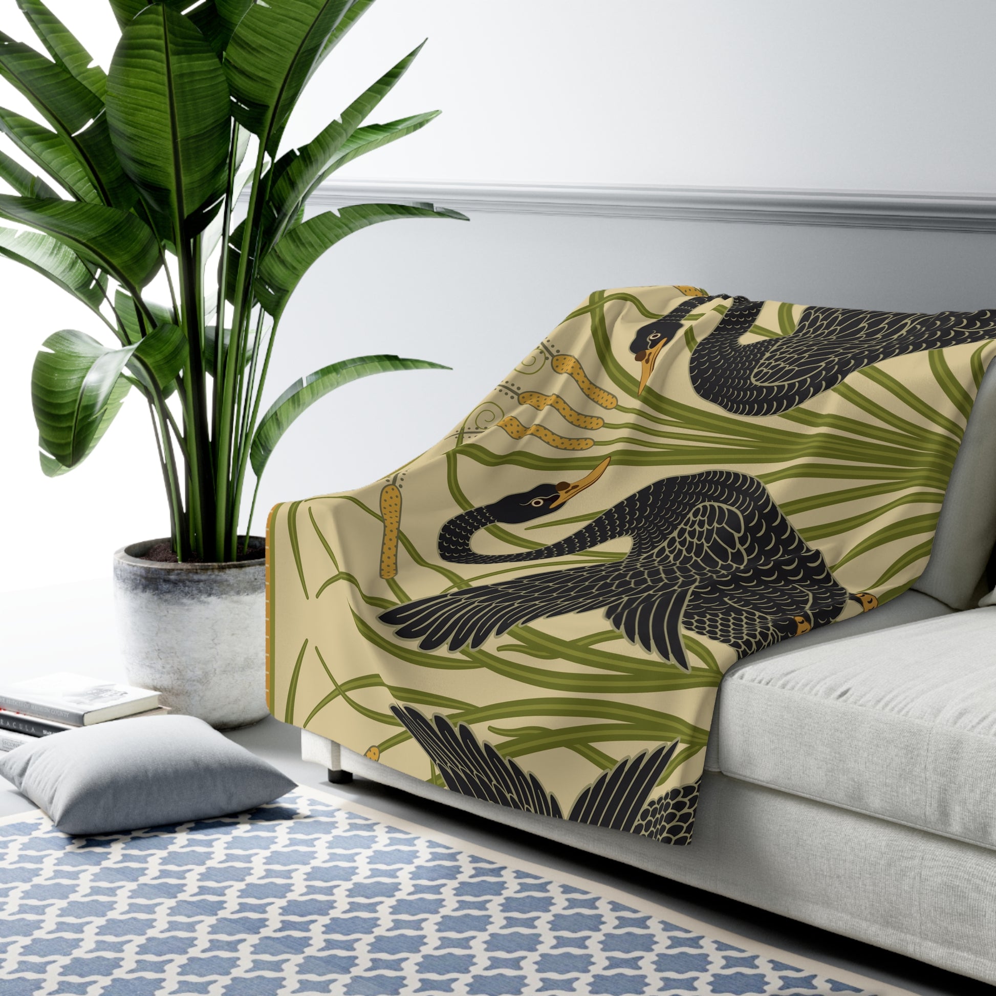 A Sherpa fleece blanket with a pattern inspired by William Morris, featuring black swans and green foliage on a beige background.