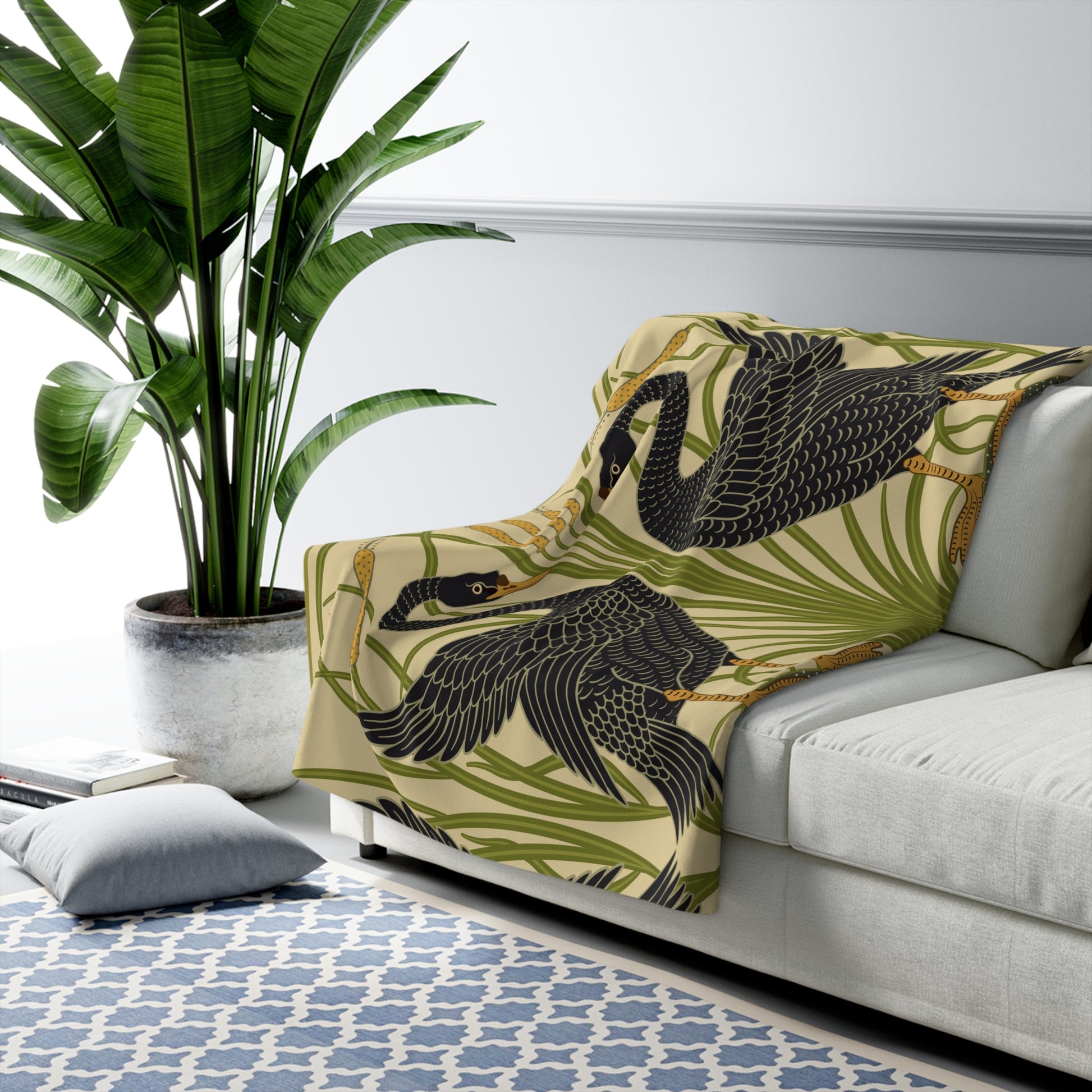 A Sherpa fleece blanket with a pattern inspired by William Morris, featuring black swans and green foliage on a beige background.
