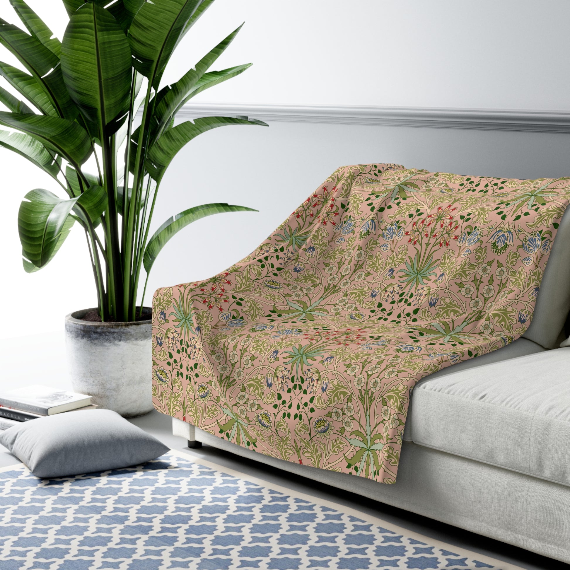 A Sherpa fleece blanket with a floral pattern in pink, green and beige colours on a pink background.