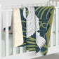 A Sherpa fleece blanket with a floral and swan William Morris & Co pattern in white and green colours on a dark background.