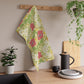 A kitchen tea towel with a floral pattern inspired by William Morris, featuring honeysuckle designs in red, yellow, and green on a light background.