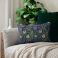A rectangular lumbar cushion with a floral William Morris & Co pattern featuring predominantly blue flowers and green leaves on a darker background.