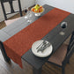 A rust-coloured table runner with a floral William Morris & Co pattern displayed on a dining table.