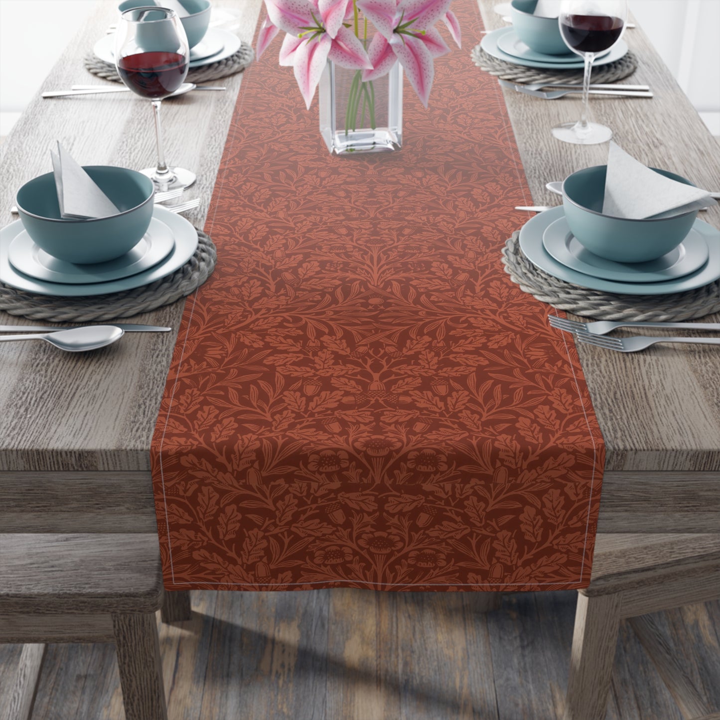 A rust-coloured table runner with a floral William Morris & Co pattern displayed on a dining table.