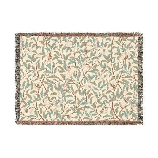 A woven cotton blanket with a geometric bird and pomegranate William Morris & Co pattern in beige, green, and brown colours, with fringed edges.