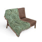 Green patterned throw blanket draped over a brown chair on a white background