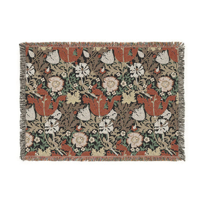 A woven cotton blanket with a geometric and floral pattern in red, green, and beige colors, with fringed edges.