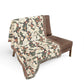 Beige patterned throw blanket draped over a brown chair on a white background