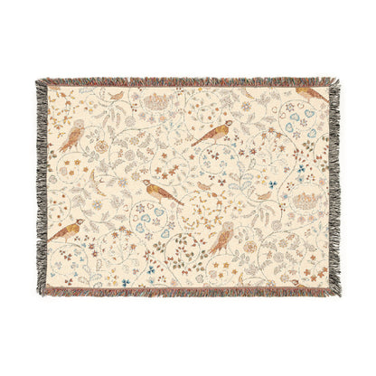 A beige woven cotton blanket with a William Morris & Co floral and bird pattern, featuring a colourful fringed edge.